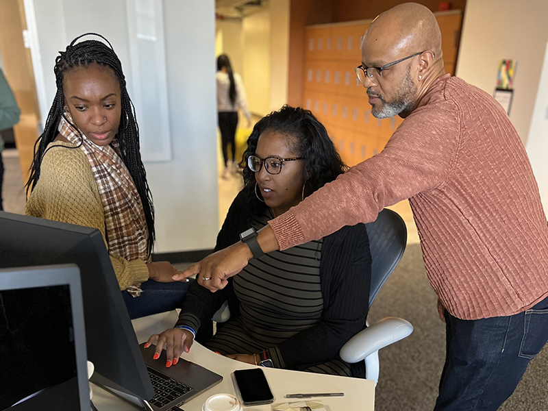 three people discussing the items on the laptop in front of them. 